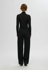 Juodos tekstūruotos ilgos rankovės palaidinė, derinama su aukšto juosmens, laisvai krentančiomis juodomis džinsomis. Džinsai turi nebaigtą apdailą ir galines kišenes.