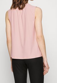 Sleeveless, pastel pink top made of soft fabric, featuring a round neckline and a relaxed fit, paired with black fitted pants.