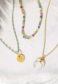 Tres collares: uno con pequeñas cuentas de turquesa y acentos dorados, otro con cuentas multicolores, y uno con una cadena dorada y un colgante en forma de media luna.