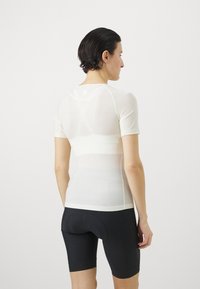 Kurze Fahrradjacke in hellem Creme, aus einem glatten, leichten Material gefertigt. Hat ein eng anliegendes Design mit kontrastierenden Nähten.