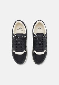 Zapatillas deportivas negras con materiales de malla y sintéticos, con detalles en blanco, cordones redondos y logo en la lengüeta.