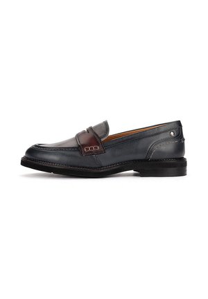 Mocasín de cuero negro con detalle de correa marrón oscuro, tacón bajo y costuras a lo largo de la suela, mostrado de lado sobre un fondo blanco.