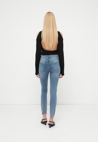  Μαύρο τοπ με ανοιχτή πλάτη, σε συνδυασμό με μπλε στενά τζιν με ξεφτισμένα τελειώματα. Το μοντέλο φοράει μαύρα σανδάλια με τακούνι, φωτογραφημένο από πίσω.