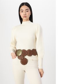 Pulover tricotat cu dungi crem, cu guler înalt, asortat cu un brâu de piele maro, cu accente circulare și nituri metalice.