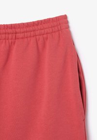 Pantalones de chándal color coral con cintura elástica, material de algodón suave, bolsillos laterales y una textura lisa, que muestran un diseño sencillo y funcional.