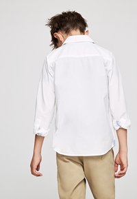 Biała koszula z długim rękawem o luźnym kroju. Posiada podwinięte mankiety z jasnoniebieskimi akcentami. Tył ma karczek i brak dodatkowych wzorów.