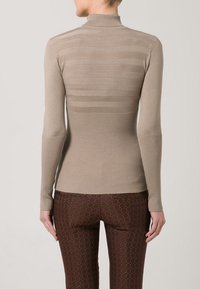 Maglietta beige a maniche lunghe dal design aderente, con costine orizzontali sulla parte superiore della schiena e colletto alto. Abbinata a leggings marroni con fantasia.
