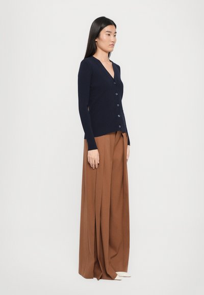 Navy ribbed cardigan with a V-neck, long sleeves, and button closure, paired with wide brown pants, set against a white background.
