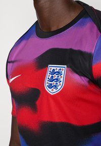 Short-sleeve jersey in purple, red, and black with abstract patterns. Features England emblem and white Nike logo on the chest.