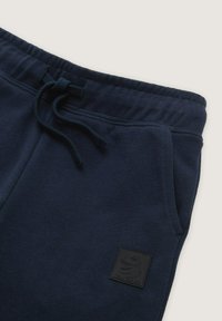 Sweat hlače tamnoplave boje, izrađene od mekanog materijala, s elastičnim strukom, vezicom, bočnim džepovima i teksturiranim logotipom.