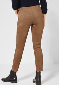 Bruna mockasinliknande smala byxor med en slät yta, med en midjehöjd vid midjan och avsmalnande ben, ihop med svarta ankelskor.