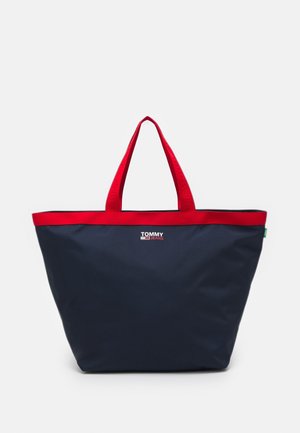 Granatowa torba na ramię z czerwonymi uchwytami i lamówką, z logo Tommy Jeans w białym i czerwonym kolorze na środku przedniej strony.