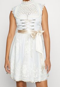 Robe sans manches bleu clair avec des accents en dentelle, un col montant, des motifs floraux brodés et une ceinture en ruban de satin à la taille.