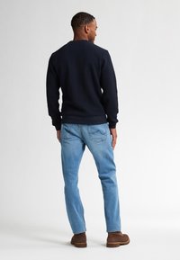 Marineblå tekstureret sweater med ribbede manchetter, parret med lyseblå jeans. Brune sko fuldender outfittet. Ingen synlige logoer eller mønstre.