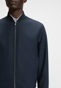 Navy bomber jacket featuring a smooth texture, high collar, and front zipper. Includes striped accents under the collar.