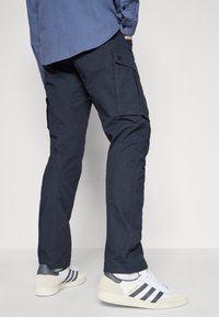 Pantaloni cargo navy din țesătură durabilă, cu buzunare laterale, croială dreaptă și cusături contrastante, asortați cu adidași albi.