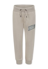 Pantalons de survêtement beige avec une taille et des poignets côtelés, dotés d'un cordon de serrage et du logo "HUGO" en vert foncé sur le côté. Tissu doux et texturé.