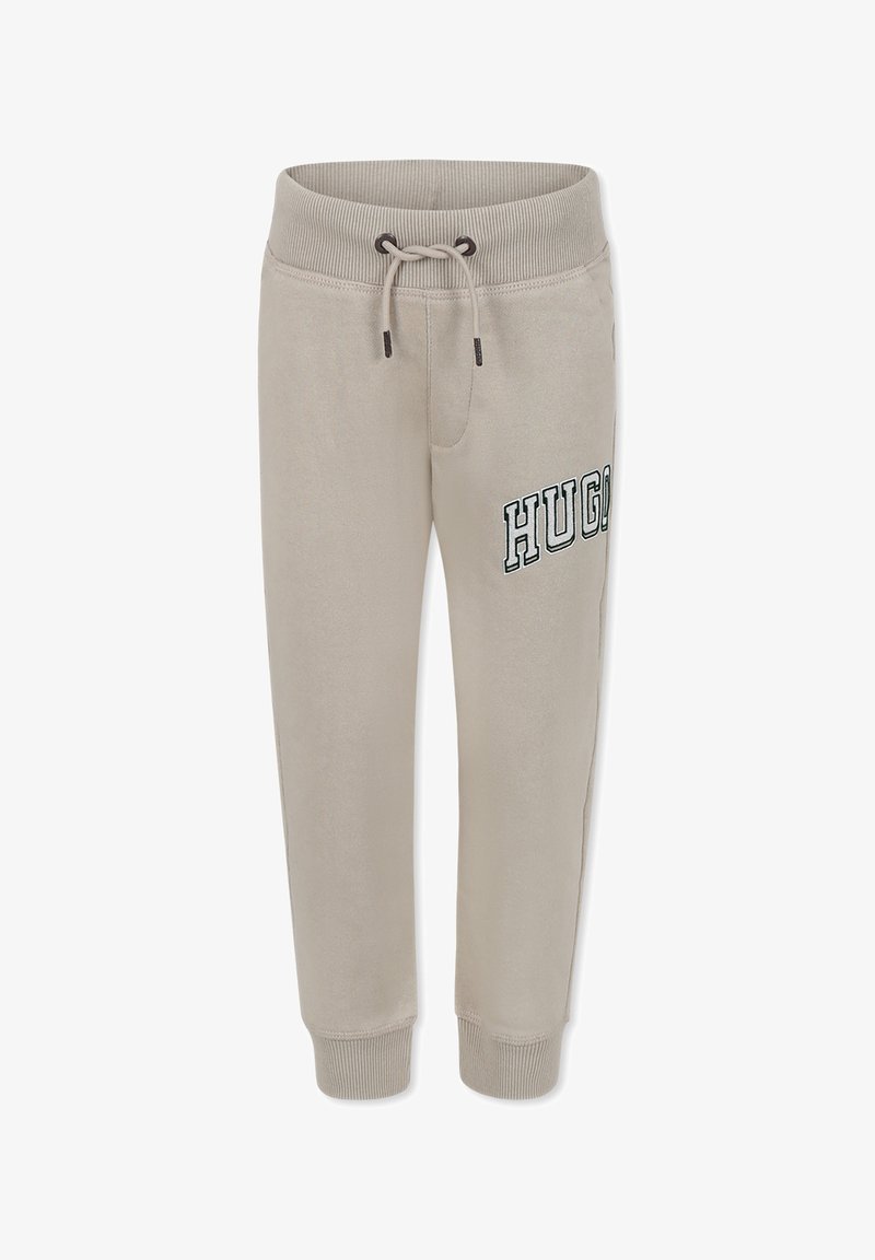 Pantalons de survêtement beige avec une taille et des poignets côtelés, dotés d'un cordon de serrage et du logo "HUGO" en vert foncé sur le côté. Tissu doux et texturé.