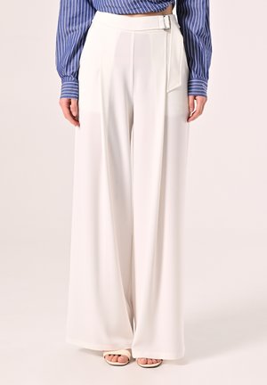 Weiße, weit geschnittene Hosen mit hohem Bund, seitlicher Schnalle, glatter Textur und sauberem Finish. Kombiniert mit einer blau gestreiften Bluse.