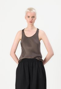Ruskea satiinitoppi, jossa on vaaleahko kaula-aukko ja leveät hihnat, yhdistettynä löysiin mustiin housuihin. Sileä pinta elegantilla kiillolla.