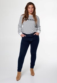Chemise rayée à manches longues avec des lignes horizontales noires et blanches, associée à un jean skinny bleu marine et des bottines beiges.