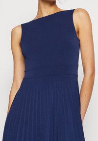 Robe sans manches bleu marine avec un design à une épaule, présentant un corsage ajusté et une texture de jupe plissée. Tissu doux et extensible.