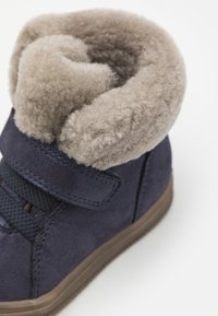 Marinblå ankelstövel med mjukt beige foder i päls, texturerad ovandel, kardborreband och gummisula som ger en tät och bekväm passform.