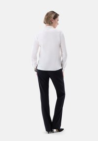 Blusa bianca a maniche lunghe con colletto, abbinata a pantaloni scuri e sartoriali. I tessuti sembrano lisci e leggeri, creando una silhouette elegante.