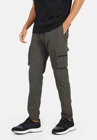 Spodnie cargo w oliwkowym kolorze o zwężanym kroju, z bocznymi kieszeniami, zamkami błyskawicznymi i wykonane z lekkiego, trwałego materiału.