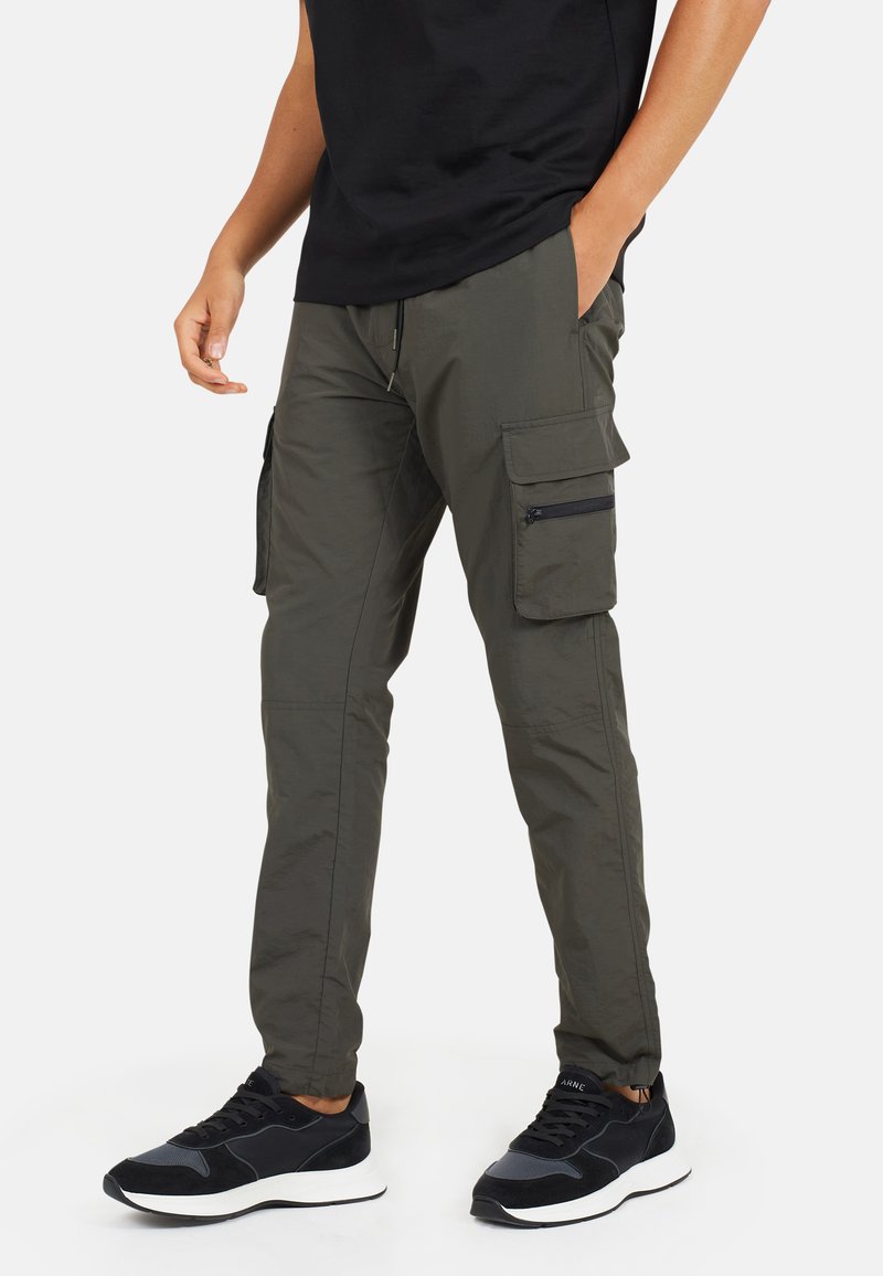 Spodnie cargo w oliwkowym kolorze o zwężanym kroju, z bocznymi kieszeniami, zamkami błyskawicznymi i wykonane z lekkiego, trwałego materiału.