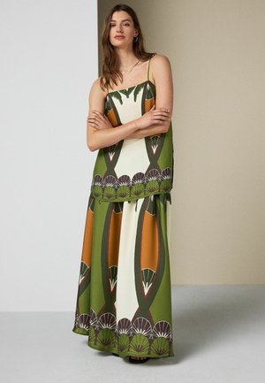 Woman standing with arms crossed wearing a green, orange, and cream patterned sleeveless top and matching wide-leg pants.