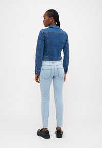 Denim jakna v modri barvi s skrajšanim dizajnom, ki vključuje gumbe in klasičen ovratnik. Usklajena z svetlimi modrimi skinny kavbojkami in črnimi čevlji.
