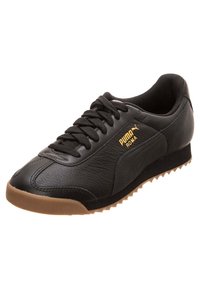 Svart Puma Roma sneaker med brun sula, överdel i läder, svarta snören och guld Puma-logotyp på sidan.