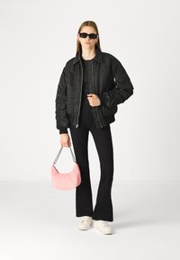 Black bomber jacket with a zip closure, paired with fitted black flared pants. Holding a pink velvet handbag with a silver chain strap.