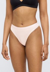 Hellrosa Tanga-Unterwäsche mit glatter Textur und elastischem Bund mit Markenlogo, vor neutralem Hintergrund präsentiert.