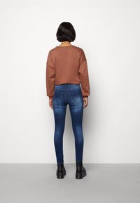 Brun löst sittande sweatshirt och mörkblå skinny jeans, med synliga sömmar och bakfickor, parat med svarta kraftiga stövlar.