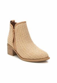 Botín de tobillo beige con textura tejida, punta afilada, tacón bajo apilado y cierre con cremallera lateral. Presenta un brillo sutil y una suela resistente.