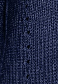 Țesătură tricotată de culoare bleumarin, prezentând un model texturat cu decupaje triunghiulare mici, uniform distribuite pe o margine. Textură moale și respirabilă.