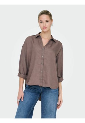 Smeđa košulja na zakopčavanje s ovratnikom, podvijenim rukavima i ležernim krojem. Tkanina izgleda mekana s suptilnom teksturom. Uparena s plavim trapericama.
