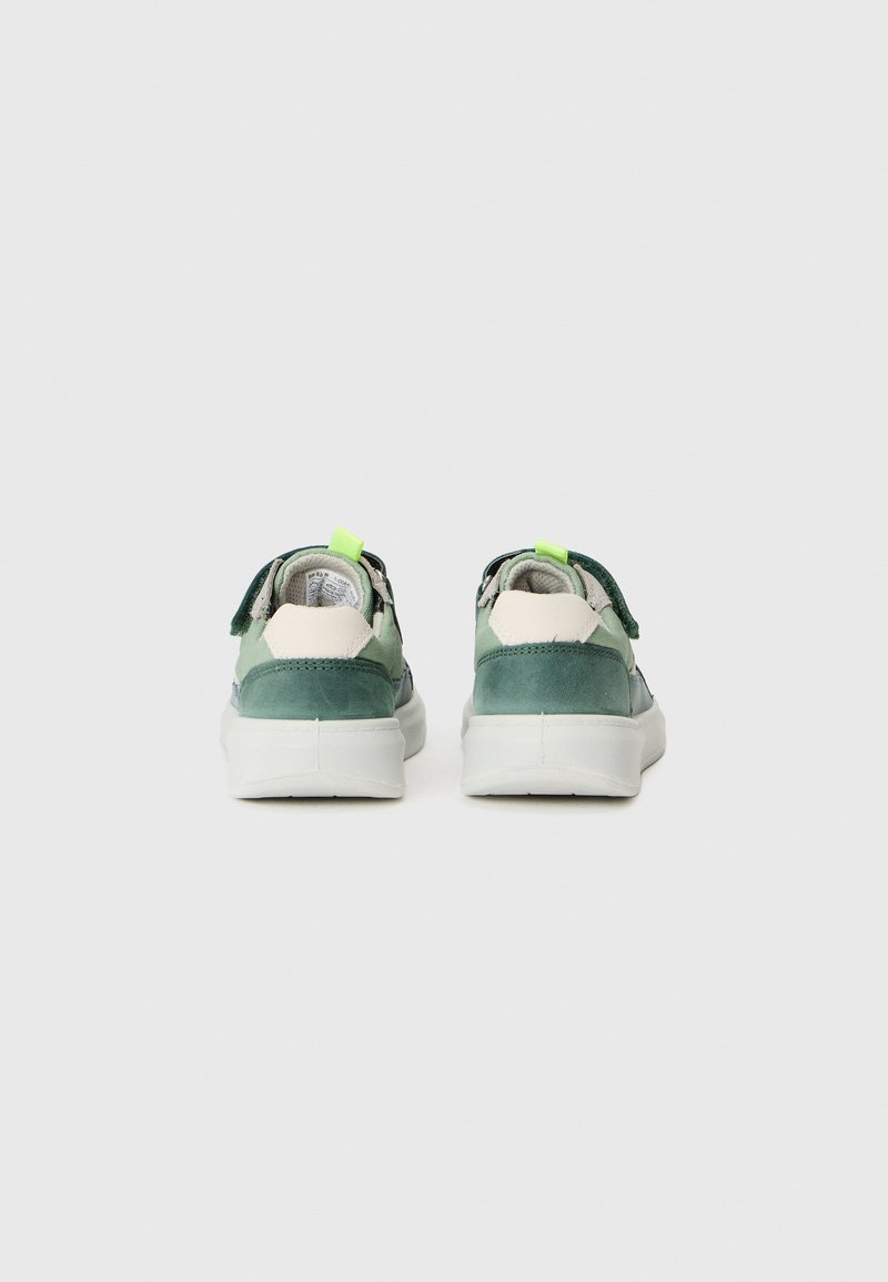 Grüne und cremefarbene Wildledersneakers mit einer weißen Sohle, ausgestattet mit einer leuchtend grünen Fersenschlaufe und einem verstellbaren Riemen. Schlichtes, modernes Design.