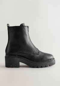 Mustad mustad nahast pahkluu saapad külgsepite ja robustse tekstuuriga kontsaga ning robustse tallaga. Omab minimaalseid õmblusi ja tõmbenööri.