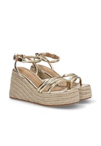 Sandalias de tiras metálicas doradas con un tacón de cuña de yute trenzado. El tacón presenta un diseño texturizado y trenzado con un forro interior beige.