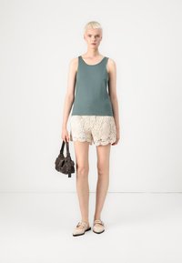 Tanktopp i teal stof, parret med cremede blonde shorts med bølgede kanter, og en brun håndtaske. Fodtøj er lyse flats.