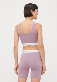 Lilla sportsbh og shorts sæt. Blødt, strækbart materiale med hvid elastisk bånd med "COPENHAGEN STUDIOS" logo på taljen. Letvægtsdesign.
