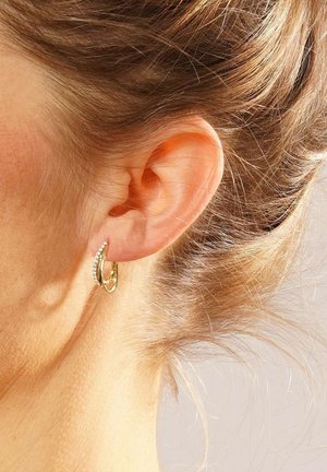Goldene Creolen mit einer glatten, glänzenden Oberfläche und kleinen, klaren Steinen, die auf einer Seite eingesenkt sind, zeigen ein modernes Design.