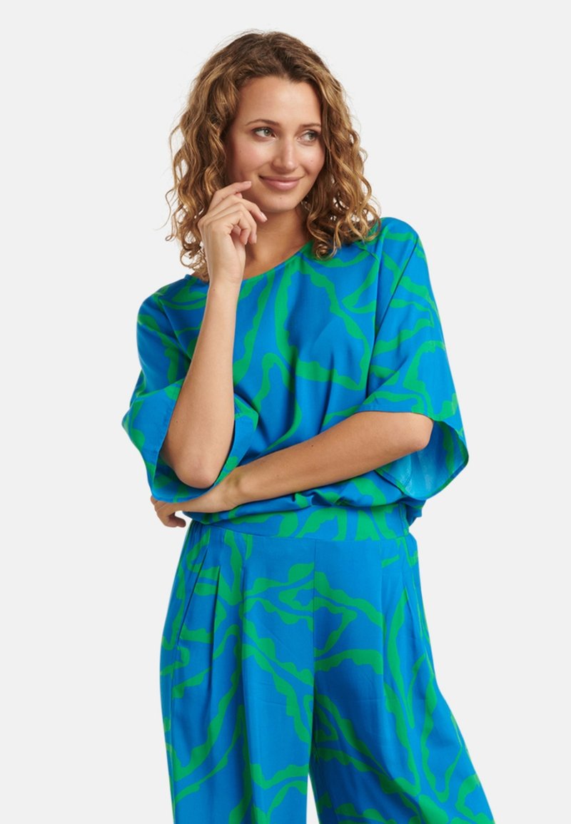 Blauw top met groen abstract patroon, brede mouwen en een losse fit, gecombineerd met bijpassende blauwe broeken, gemaakt van lichtgewicht stof.