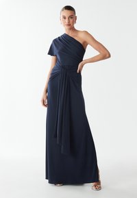 Abito lungo blu navy con spalla unica realizzato in tessuto liscio, caratterizzato da un design drappeggiato, vita annodata e silhouette fino al pavimento con uno spacco laterale.