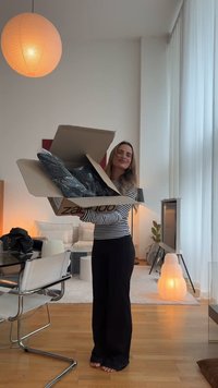 Scatola di cartone Zalando aperta, che rivela abbigliamento nero in plastica. Una persona indossa una maglietta a righe con maniche lunghe e pantaloni neri, mentre si trova all'interno.