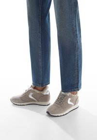 Sneaker in suede grigio chiaro con accenti argento, dotati di un colletto soffice, soletta imbottita e suola in gomma nera. Abbinati a jeans blu.