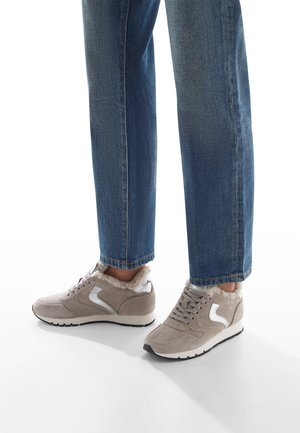 Sneaker in suede grigio chiaro con accenti argento, dotati di un colletto soffice, soletta imbottita e suola in gomma nera. Abbinati a jeans blu.